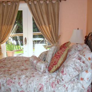 A cozy bedroom interior with floral bedding and draped curtains framing French doors.