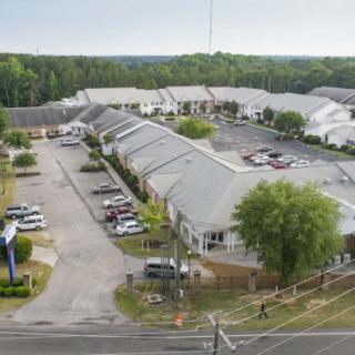 Aerial view of a commercial area with buildings, a parking lot, and trees in the surroundings.
