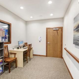 A small office space with a desk, chairs, and a computer facing a wooden door.