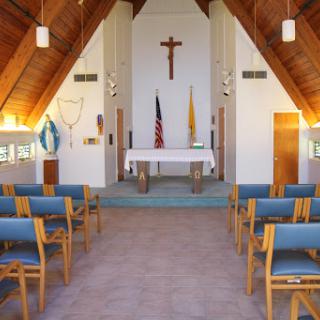 A serene interior view of a church featuring an altar, wooden beams, and rows of blue chairs.