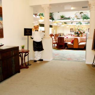 A chef stands at the entrance of a warmly decorated restaurant, inviting guests into the dining area.