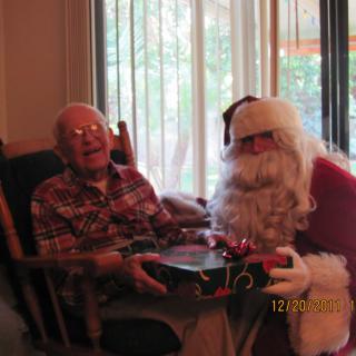 An elderly person receives a gift from someone dressed as Santa Claus during a holiday celebration.