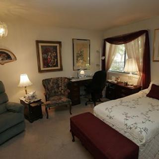 A cozy and traditional bedroom setup with a bed, desk, armchair, and decorative elements.