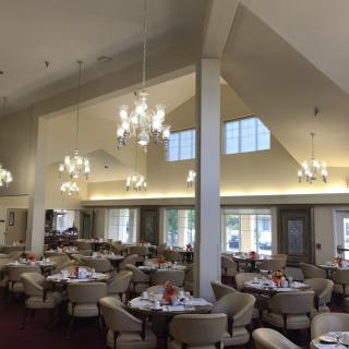 A spacious dining area with elegant chandeliers, round tables, and comfortable seating.