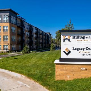 A modern apartment building with a sign reading 'Hilltop on Main Apartments' and 'Legacy Commons'.