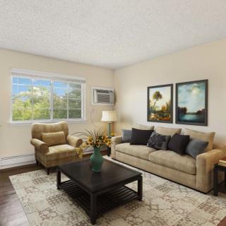 A cozy living room featuring a beige couch and armchair, a dark coffee table, decorative pillows, and two framed artworks on the wall.