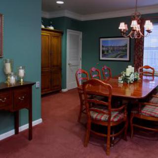 A cozy dining room with green walls, featuring a wooden table and chairs, a chandelier, and decorative elements.