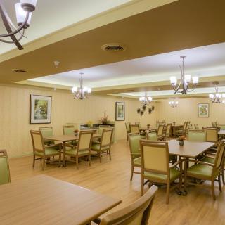 An empty dining room with neatly arranged tables and chairs, featuring elegant chandeliers and a wooden floor.