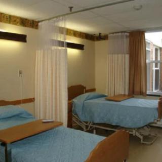 A hospital room with two patient beds separated by privacy curtains.
