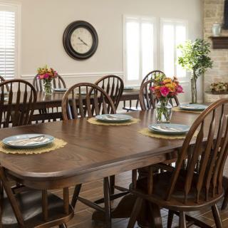 A cozy dining room with a wooden table set for a meal, featuring floral centerpieces and wooden chairs.