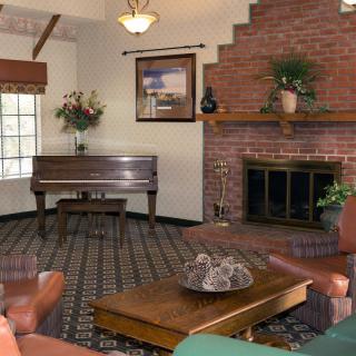 A cozy living room featuring a piano, a brick fireplace, and comfortable furniture.