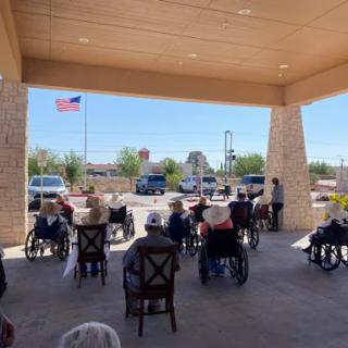 Seniors gathered in outdoor seating for an event, with a flag waving in the background.