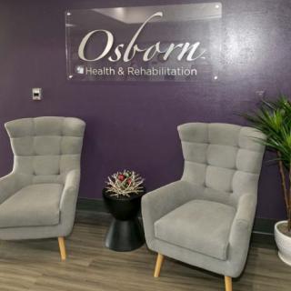 A cozy waiting area with two grey chairs, a small table with a succulent, and a potted plant against a purple wall.