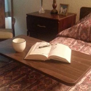 A cozy setup with a book and coffee on a bed tray next to a nightstand.