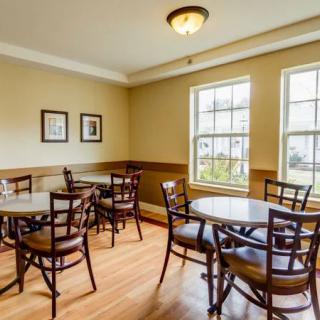 Cozy cafe interior with wooden tables and chairs, brightened by natural light from large windows.
