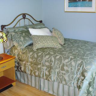 A cozy bedroom with a neatly made bed adorned with pillows and a nightstand holding a lamp.