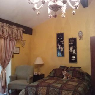 A cozy bedroom with warm yellow walls, a decorative chandelier, and an upholstered armchair.