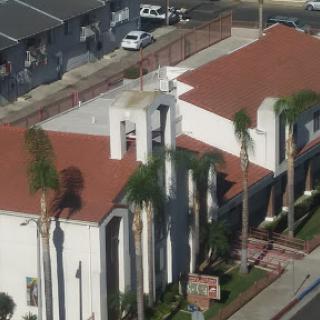 Aerial view of a building with red rooftops surrounded by palm trees.