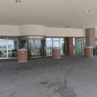 The entrance of a modern building featuring glass doors and a spacious parking area.