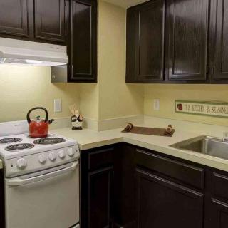 A small kitchen with dark cabinets, a white stove, and a stainless steel sink.
