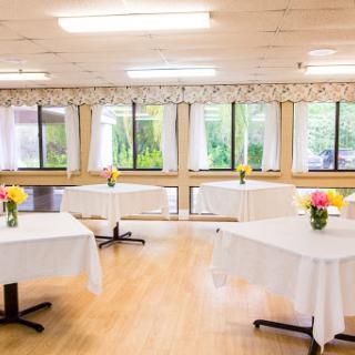 A well-lit event space featuring neatly arranged tables with flower centerpieces, perfect for gatherings and celebrations.