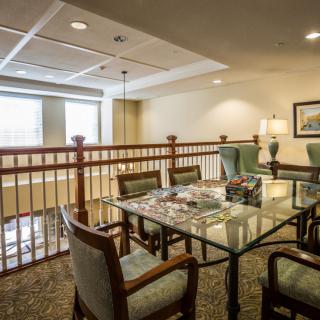 A cozy interior space featuring a table and chairs set, with a view of the railing and windows.