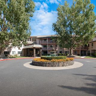 A well-landscaped building entrance with a roundabout, surrounded by trees under a partly cloudy sky.