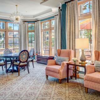 A spacious and elegantly decorated living room with traditional furniture, featuring large windows, a dining area, and a chandelier.