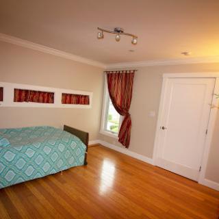 A cozy bedroom featuring a bed with a turquoise cover, elegant curtains, and wooden flooring.