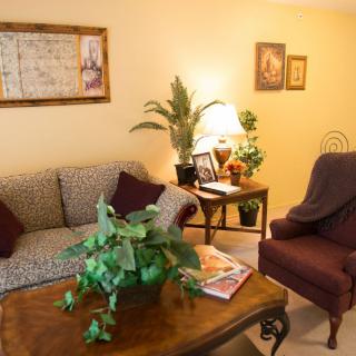 A cozy living room featuring a sofa, armchair, and coffee table with indoor plants and decor.