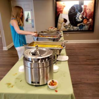 A woman serves food from a buffet setup during an event, showcasing a variety of dishes.