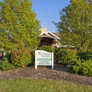 A building surrounded by lush greenery and a sign out front on a sunny day.
