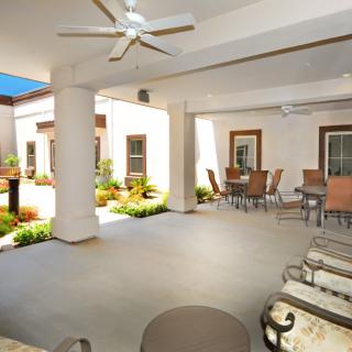 A spacious outdoor patio with comfortable seating and a ceiling fan, overlooking a garden.