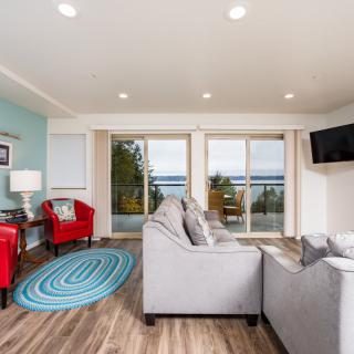 A modern living room with bright natural light, featuring comfortable furniture and a scenic lake view through sliding doors.