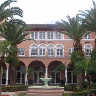 A Mediterranean-style building with arches and palm trees lining the entrance.