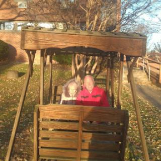 A couple enjoying a sunny day on a wooden swing in the park.