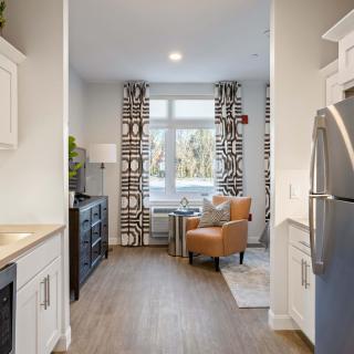 A modern kitchen with light-colored cabinets, a refrigerator, and a cozy seating area by the window.