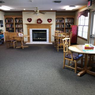 A cozy library reading room with tables, chairs, and a fireplace surrounded by bookshelves.