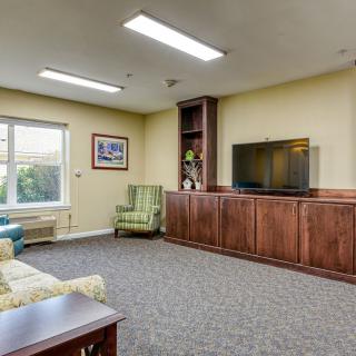 A cozy living room with a television, couch, armchair, and large window.