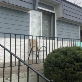 A small porch with a chair, railing, and bushes in front of a house.