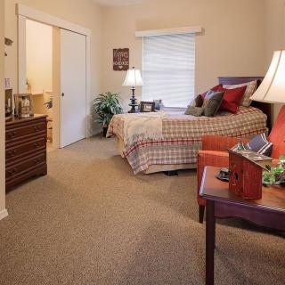 A cozy bedroom with a neatly made bed, warm lighting, and comfortable furniture.