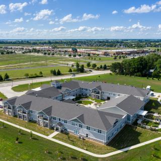 Aerial view of a large residential building surrounded by greenery and open fields under a partly cloudy sky.