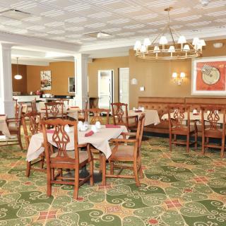 A well-furnished dining area with wooden tables and chairs, adorned by a chandelier and patterned carpet.