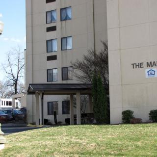 Entrance to a residential apartment building with a visible sign and surrounding greenery.