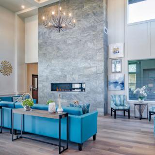 A modern living room featuring a high ceiling, marble fireplace, and blue sofas.