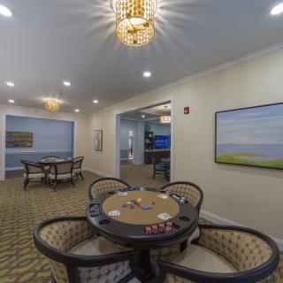 A well-furnished interior room featuring a round card table with chairs, elegant chandeliers, and wall artwork.