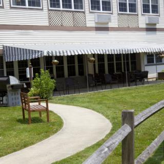 A building with an awning covering outdoor seating and a landscaped lawn in front.