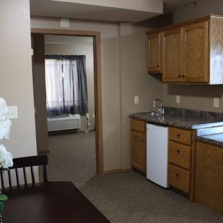 A small kitchen area in an apartment with wooden cabinets and a view into another room.