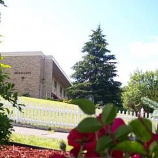 A scenic view of a building with a white fence, surrounded by trees and colorful flowers.