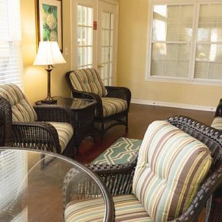 A cozy living room with striped cushioned chairs and a glass table, softly lit by a lamp.
